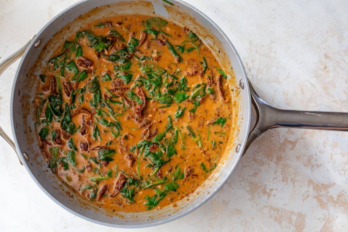 Creamy sauce with spinach and sun-dried tomatoes in a skillet.