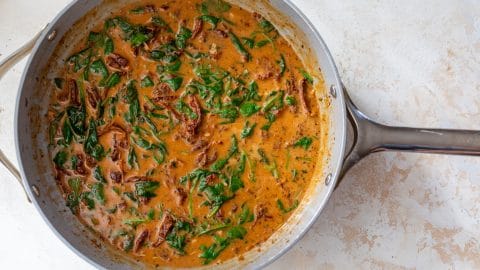 Creamy sauce with spinach and sun-dried tomatoes in a skillet.