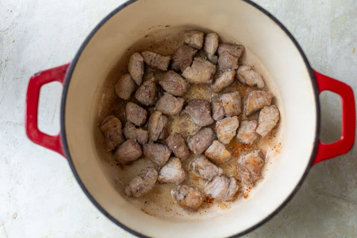 Browning chunks of pork in a red enameled cast iron pot.