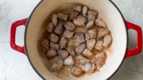 Browning chunks of pork in a red enameled cast iron pot.