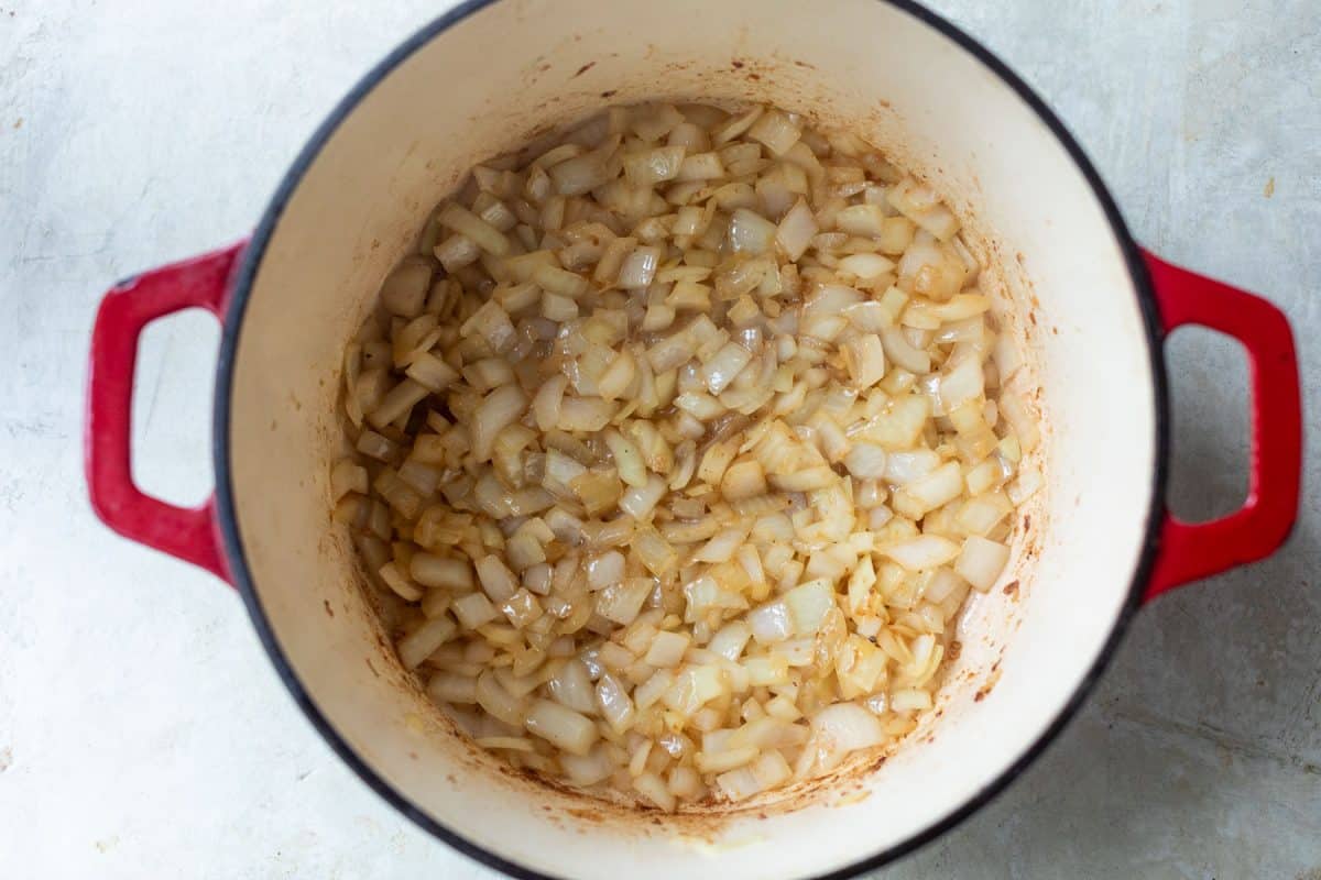 Chopped onions sautéing in a red enameled cast iron pot.