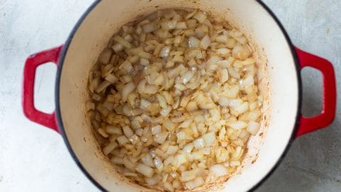 Chopped onions sautéing in a red enameled cast iron pot.