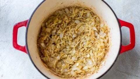 Chopped onions and shredded vegetables sautéing in a red enameled cast iron pot.