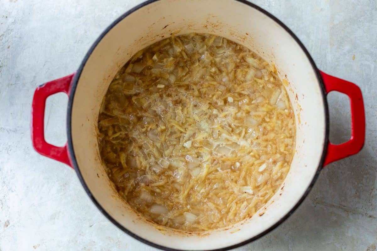 Chopped onions sautéing in a red enameled cast iron pot.