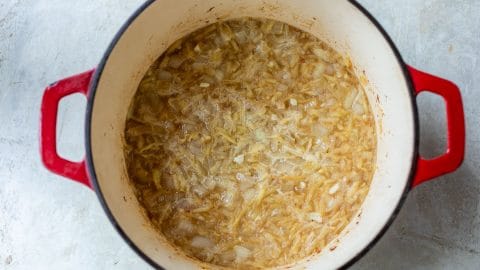 Chopped onions sautéing in a red enameled cast iron pot.