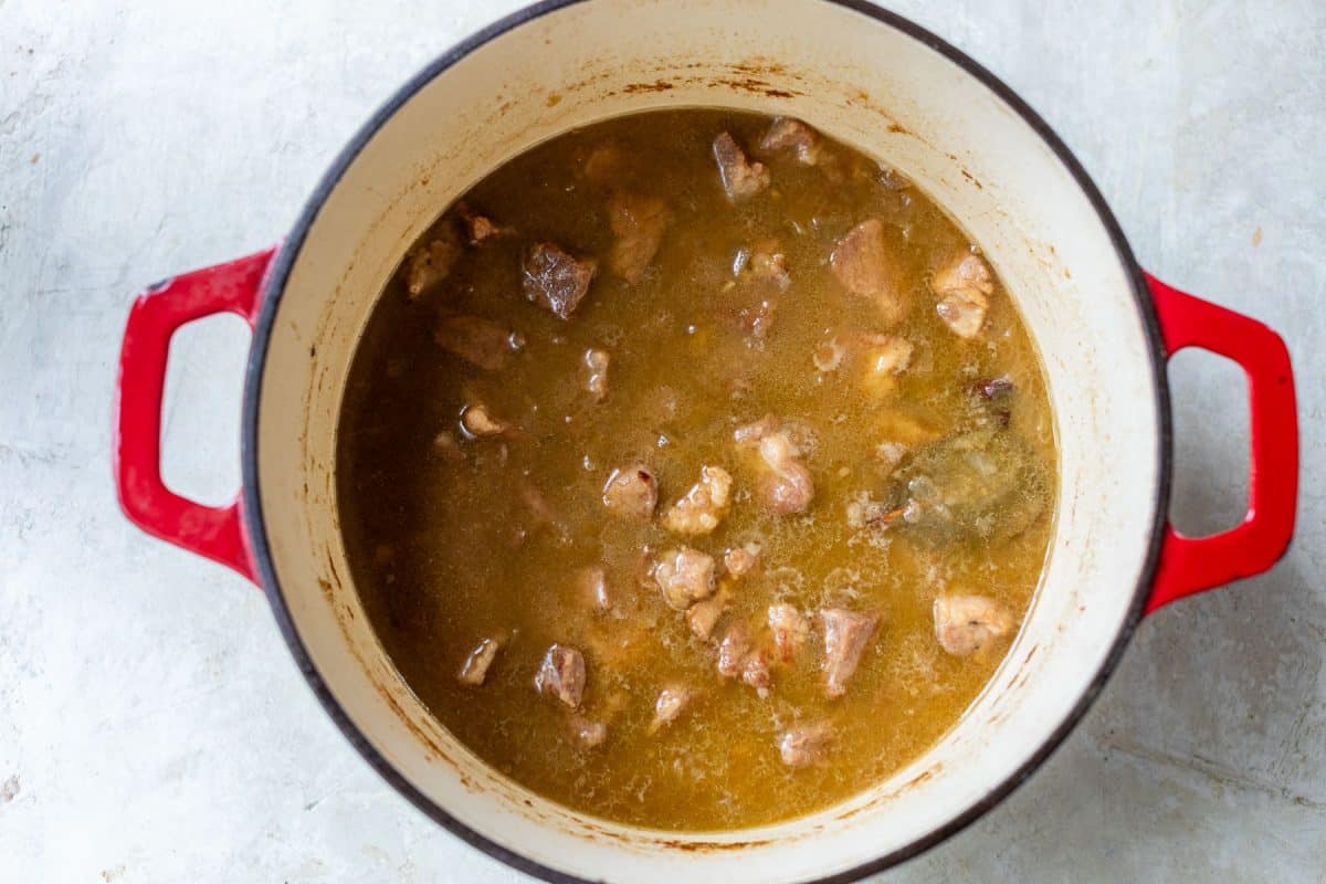 A red enameled cast iron pot filled with a pork stew in broth.