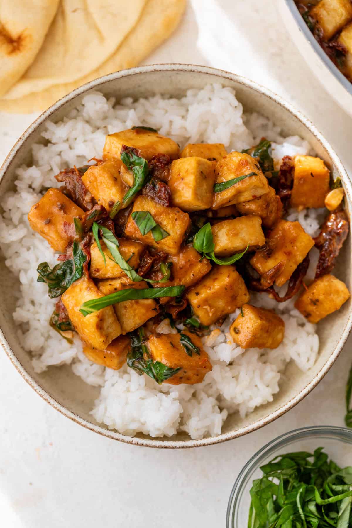 A bowl of white rice topped with cubed marry me tofu in a creamy sauce with herbs, served with flatbread.