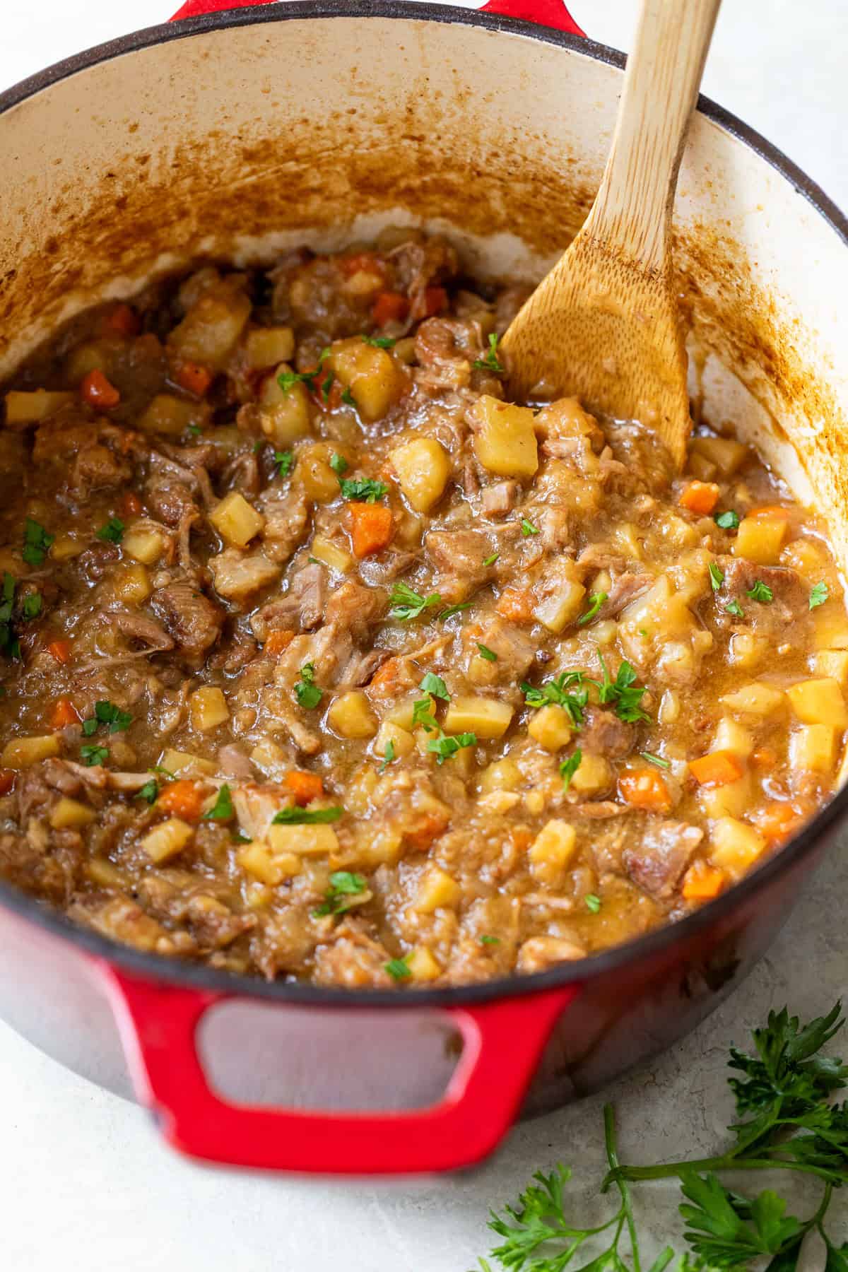 Pork stew in a red enameled cast iron pot with a wooden spoon.