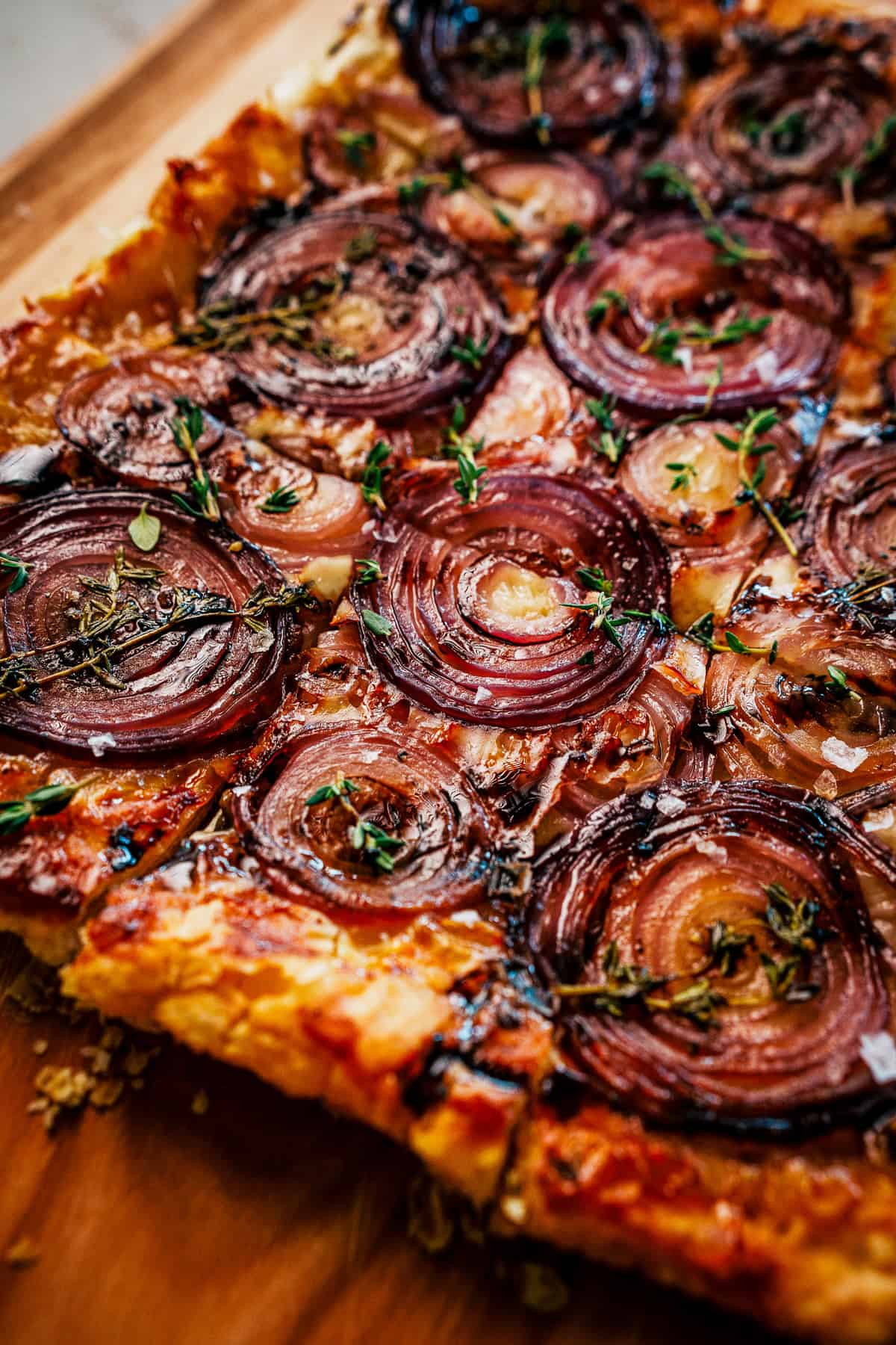 Savory tart topped with caramelized onion slices and fresh thyme herbs.